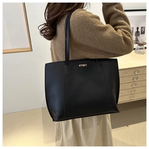 Close-up of a black leather tote bag with a front pocket and silver bar detail on shoulder