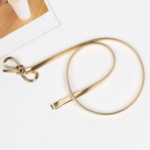 Macro detail of golden elastic metal belt featuring a stylish bow buckle on a white surface