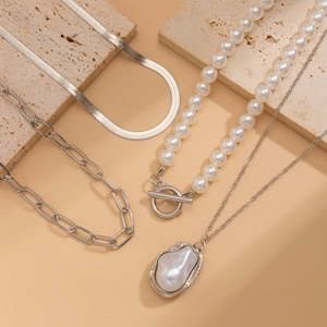 Macro view of silver snake chain and paperclip necklace with baroque pearl pendant set