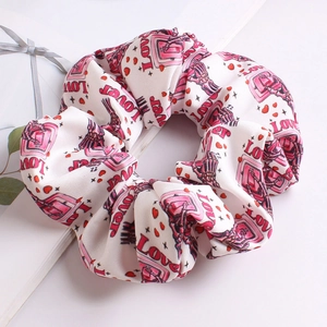 Close-up of white scrunchie with pink LOVE print and soft fabric texture detail