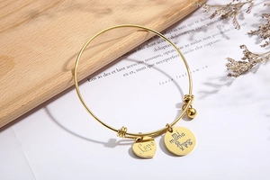 Detailed shot of golden heart and Mi Mama pendants on adjustable steel bangle