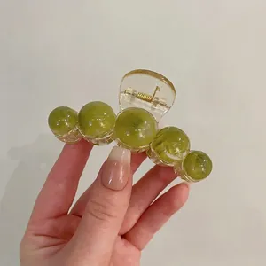 Detail of green acrylic hair claw clip featuring five marbled spherical beads on a gold spring