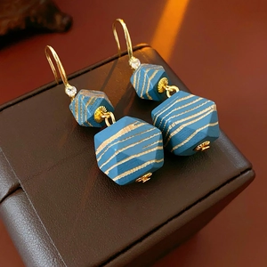 Close-up of bohemian earrings featuring blue hexagonal beads with gold stripes and crystals