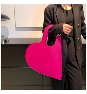 Model posing with large hot pink felt heart-shaped tote bag against a black background