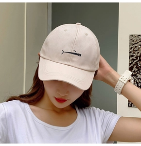 Detail of whale embroidery on beige cotton baseball cap worn by a female model