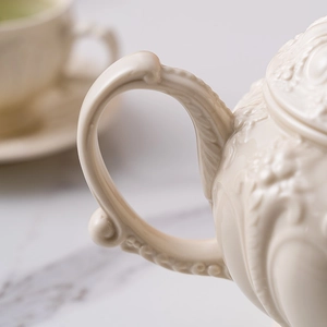Macro shot of cream ceramic teapot handle with vintage embossed floral textures