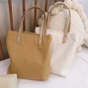 Close-up of canvas tote bag featuring brown faux leather straps and metal rivet details