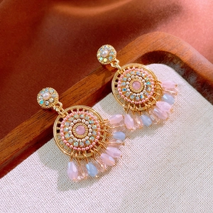 Close-up of bohemian gold tassel earrings with pink and blue beads on a linen tray