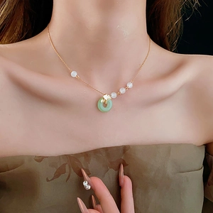 Close-up of gold ginkgo leaf and green peace buckle pendant necklace on model neck