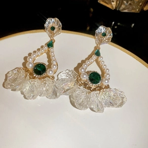 Detail of drop earrings with emerald stones and pearls on white ceramic surface