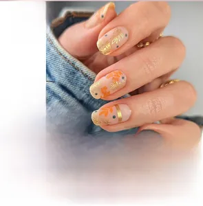 Detail of square press-on nails with gold leaf patterns and blue dots on pink base