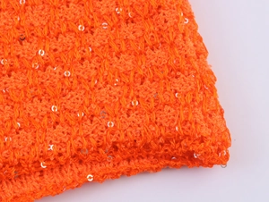 Details von orangefarbenem Strickstoff mit silbernen Pailletten und Textur
