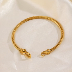 Golden twisted cable bracelet with horseshoe hook clasp on white satin background
