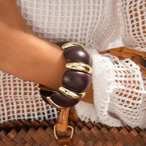 Detail of dark brown acrylic and gold metal link bracelet on model's wrist