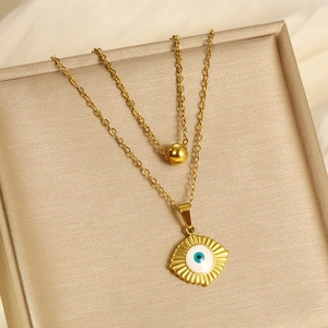 Detail of double-layer gold necklace featuring evil eye pendant and gold bead accents