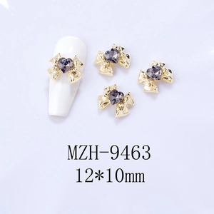 Detailed view of alloy bow nail charm with a heart-shaped rhinestone on a white nail tip