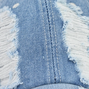 Detailed macro view of distressed blue denim fabric with white stitching and frayed edges