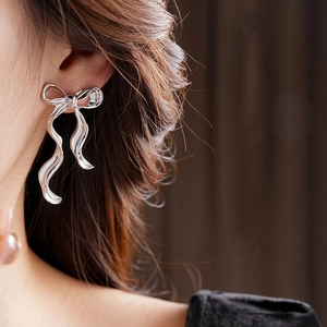 Gros plan de boucles d'oreilles nœud argentées portées, montrant une texture métallique