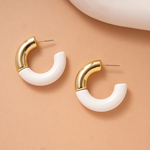 Detail of gold and white acrylic C-shaped hoop earrings on a peach background