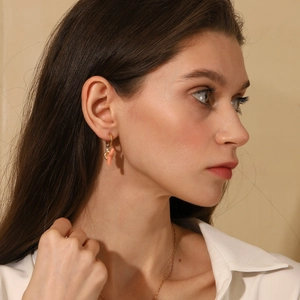 Close-up of a model wearing a 18K gold plated earring with a pink coral stone pendant