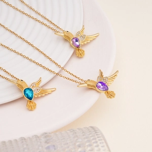 Elegant gold hummingbird necklace with purple and blue crystals on white textured tray
