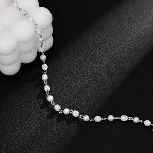 Close-up of silver chain with white pearls and sparkling rhinestone sphere beads on leather