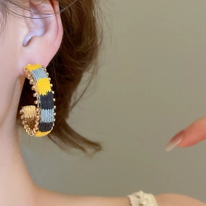 Macro shot of colorful woven cotton cord wrapped around a C-shaped gold hoop earring