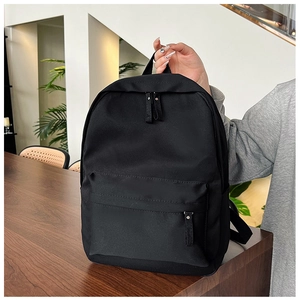 Minimalist black canvas backpack showing front zipper pocket and top handle detail