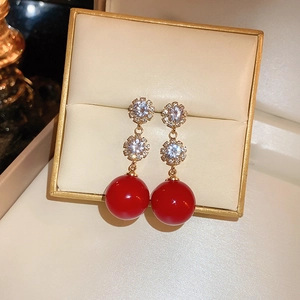 Detailed shot of New Year red zircon and faux pearl drop earrings on beige leather case