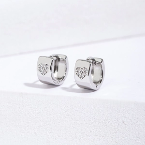 Macro shot of silver huggie earrings with heart-shaped pavé zircon and hinge design