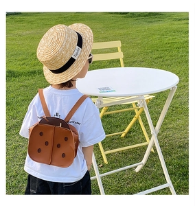 Outdoor back view of a cute brown leather ladybug backpack for toddlers in a park