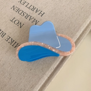 Close-up of cloud-shaped acetate hair claw with blue and pink marble textures on a vintage book