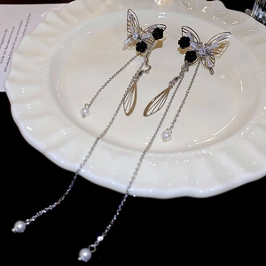 Detail of long butterfly tassel earrings with black rose, pearl charm on white ceramic tray