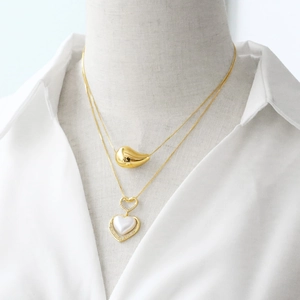 Gold layered necklace set with a bean pendant and a pearl heart pendant on a model