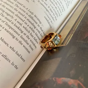 Detail of vintage gold ring with rectangle blue gemstone and amber stones on an open book