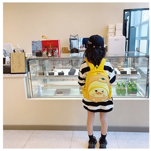 Little girl wearing a yellow cartoon duck backpack in a modern cafe setting