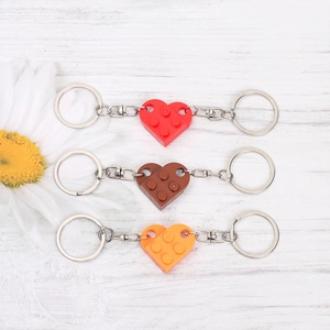 Detail of red and orange interlocking heart brick keychains on white wood background