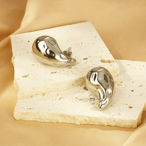 Vue macro de boucles d'oreilles goutte argentées avec texture ondulée sur soie