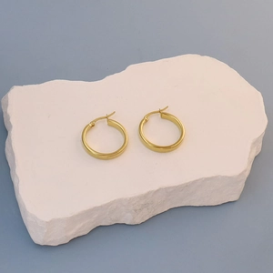 Detail of chunky gold hoop earrings with secure clasp on a white marble texture stone