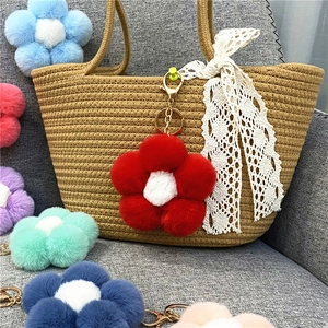 Detailed view of colorful plush flower pompom keychain charms hanging on a woven bag