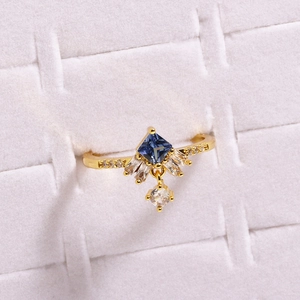 Macro detail of a gold ring featuring a square blue stone and dangling white cubic zirconia