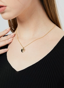 Close-up of golden necklace featuring a heart pendant with a detailed wing design on model