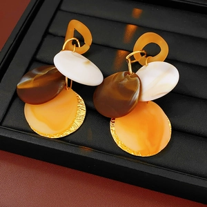 Close-up of geometric layered resin earrings with textured gold discs on black display