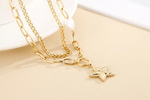 Detail of gold double-layer necklace with star pendant and heart pearl on chunky chain