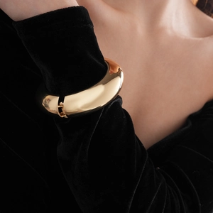 Close-up of a chunky gold cuff bracelet with mirror finish on a black velvet sleeve