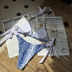 Détail du haut de bikini imprimé serpent bleu avec chaîne dorée sur des journaux