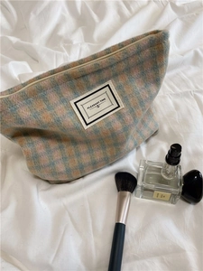Close-up of pink and blue plaid tweed cosmetic bag on bed with perfume and brush