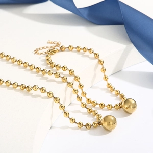 Golden stainless steel bead chain necklace with polished sphere pendant on white stand