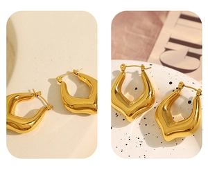 Detailed macro view of golden geometric C-shaped earrings on a ceramic display