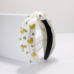 Détail d'un bandeau en tissu blanc noué avec des breloques bananes et des strass
